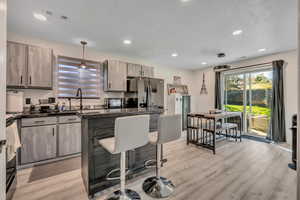 Kitchen featuring dark countertops, hanging light fixtures, a kitchen breakfast bar, black appliances, and recessed lighting