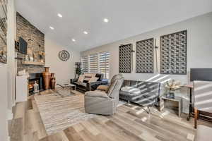 Living room featuring recessed lighting, high vaulted ceiling, light wood finished floors, and a stone fireplace