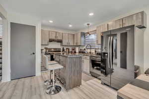 Kitchen with black appliances, a kitchen bar, a kitchen island, light wood-type flooring, and dark countertops