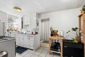 Kitchen featuring white cabinets, freestanding refrigerator, white gas stove, light tile patterned floors, and tasteful backsplash