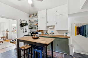 Kitchen with open shelves, white cabinetry, green cabinetry, butcher block counters, and stainless steel range with electric stovetop