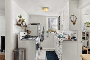 Kitchen with white appliances, white cabinets, tile counters, light tile patterned floors, and open shelves