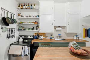 Kitchen featuring green cabinetry, electric stove, and open shelves