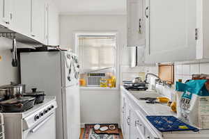 Kitchen featuring tile counters, white cabinetry, tasteful backsplash, white appliances, and crown molding