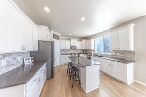 Kitchen with breakfast bar/island, white cabinets, tile backsplash, stainless steel appliances, and light wood-style floors