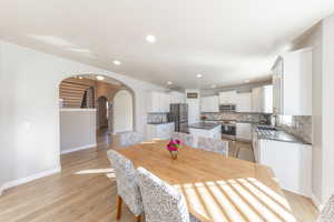 Dining area featuring light wood-style floors, arched walkways, and recessed lighting