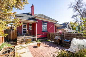 Back of house featuring brick siding, a chimney, a patio area, and a shingled roof