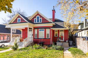Victorian-style house with a chimney, a porch, a shingled roof, and a front yard