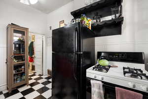 Kitchen with white gas range, tile patterned floors, freestanding refrigerator, and wainscoting
