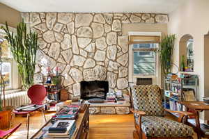 Sitting room with a stone fireplace, wood finished floors, and radiator heating unit