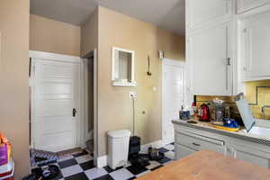 Kitchen with tile patterned floors, tasteful backsplash, light countertops, and white cabinets