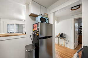 Kitchen featuring freestanding refrigerator, light wood-style floors, stove, and white cabinets