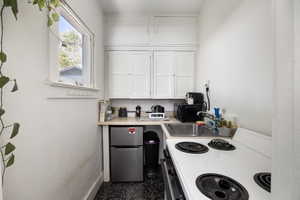 Kitchen featuring white range with electric stovetop, white cabinets, light countertops, freestanding refrigerator, and black microwave