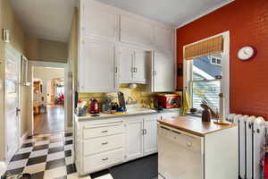Kitchen featuring radiator, light flooring, light countertops, white cabinetry, and dishwasher