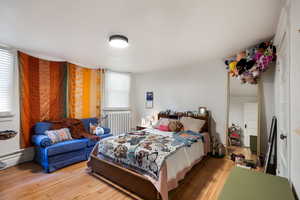 Bedroom with wood-type flooring and radiator heating unit