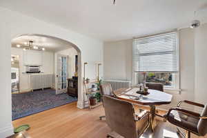 Dining room with radiator heating unit, wood-type flooring, arched walkways, and a textured wall
