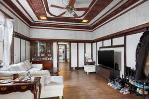 Living room featuring ceiling fan, a high ceiling, a decorative wall, and wood finished floors