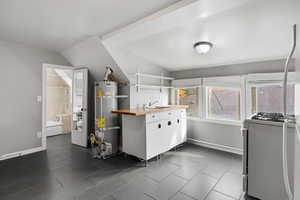 Laundry room with secured water heater, lofted ceiling, a wall mounted air conditioner, and dark tile patterned flooring