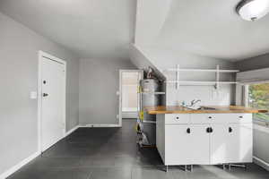 Kitchen featuring white cabinets, wooden counters, secured water heater, open shelves, and dark tile patterned flooring