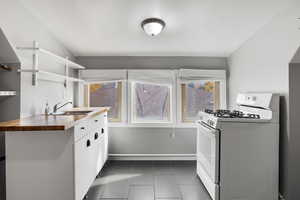 Kitchen with white gas stove, white cabinetry, dark tile patterned flooring, and open shelves