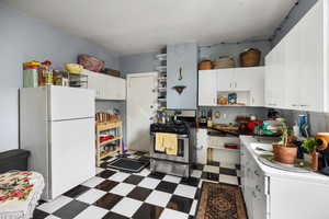 Kitchen featuring dark flooring, open shelves, freestanding refrigerator, white cabinetry, and gas range