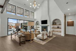 Living area with built in features, hanging lights, dark wood-style flooring, a large fireplace, and a high ceiling
