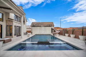 Integrated pool / hot tub featuring a patio, a water slide, and a fenced backyard