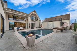 Combined pool / hot tub featuring a water slide, a patio, and an outdoor living space with a fire pit