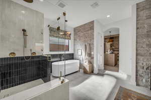 Primary Suite bath featuring tiled shower, tile walls, a freestanding tub, washer dryer combo