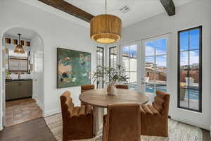 Dining space featuring arched walkways, beamed ceiling, and wood finished floors