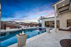 Pool at dusk with a water slide, a patio, a fenced backyard, and an outdoor fire pit