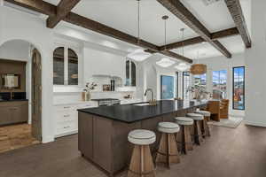 Two tone kitchen with a kitchen island with sink, glass fronted cabinets, a breakfast bar area, arched walkways, and hanging light fixtures