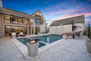 Integrated pool / hot tub featuring a water slide, a patio area, an outdoor living space with a fire pit, and a balcony