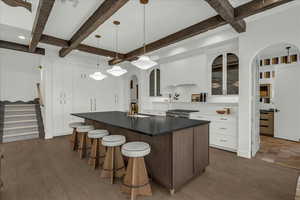 Kitchen featuring glass insert cabinets, arched walkways, an island with sink, a breakfast bar area, and pendant lighting