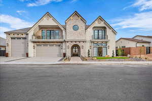 French provincial home with a balcony, stone siding, french doors, and decorative driveway