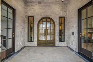 View of exterior entry featuring french doors, stone siding, and a patio