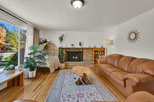 Living area featuring a textured ceiling, a stone fireplace, and light wood-style floors