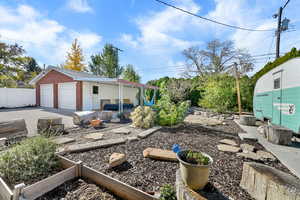 View of side of property featuring an outdoor structure, a garden, brick siding, and a patio
