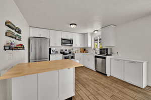 Kitchen with stainless steel appliances, white cabinetry, butcher block countertops, a textured ceiling, and wood finish floors