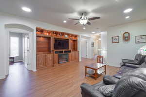 Living area with arched walkways, LVP light wood-style flooring, ceiling fan, recessed lighting, and a glass covered fireplace