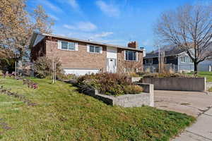 Bi-level home featuring brick siding, a chimney, and an attached garage