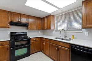 Kitchen featuring black appliances, backsplash, brown cabinets, under cabinet range hood, and a textured ceiling