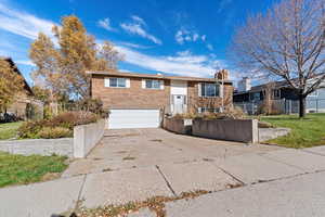 Bi-level home featuring driveway, brick siding, an attached garage, and a chimney