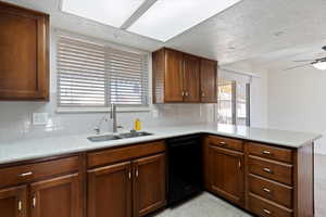 Kitchen featuring dishwasher, backsplash, a peninsula, ceiling fan, and light stone countertops