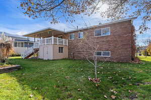 Back of house with stairway, a yard, brick siding, and shed under covered deck.