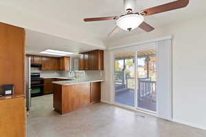 Kitchen featuring a peninsula, Wood brown cabinetry, gas stove, ceiling fan, and under cabinet range hood