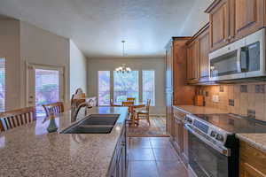 Kitchen featuring stainless steel appliances, a textured ceiling, decorative light fixtures, dark stone counters, and dark tile patterned floors