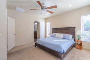 Bedroom with ensuite bath, light colored carpet, recessed lighting, arched walkways, and a ceiling fan