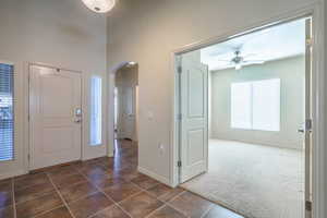 Entryway featuring dark carpet, arched walkways, dark tile patterned floors, and a ceiling fan