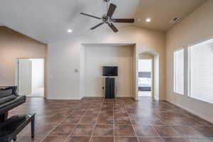 Living area with lofted ceiling, ceiling fan, arched walkways, dark tile patterned flooring, and a textured ceiling